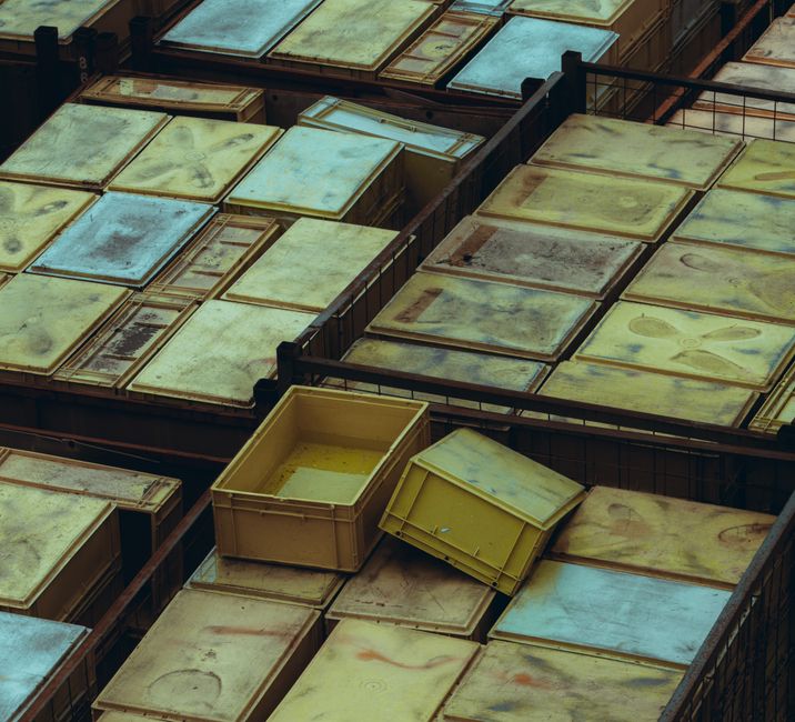 A collection of large, rectangular wooden frames and panels, predominantly in shades of weathered beige, cream, and light blue, stacked and arranged inside a warehouse or storage facility. The frames